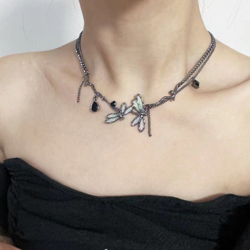 Necklace with leaf-like pendants and black stones worn by a person against a neutral background