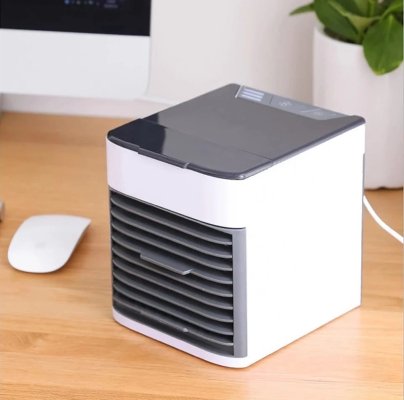 Small portable air conditioner fan on a desk with a computer monitor and plant in the background